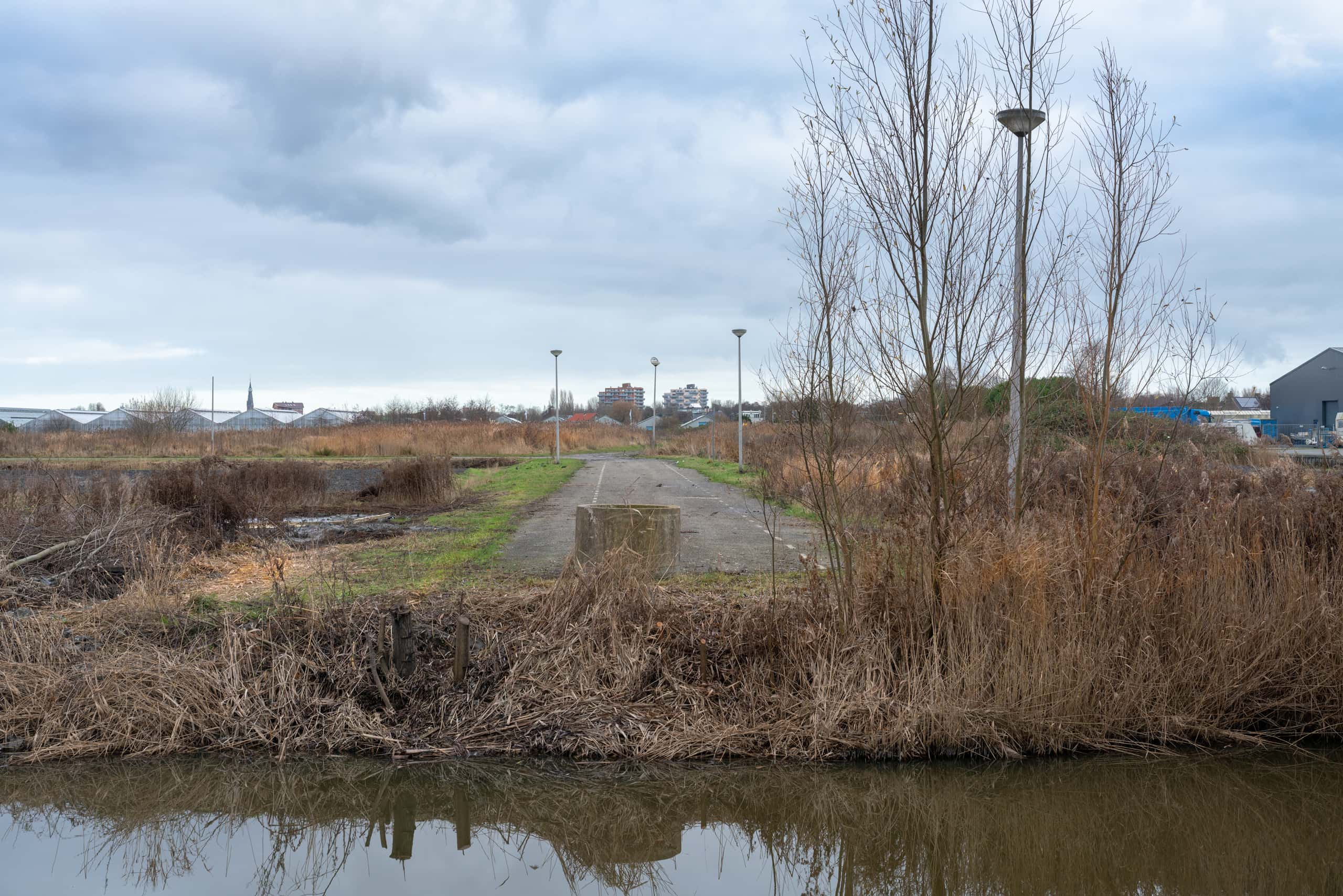 Water met daarachter een autoweg, een grasveldje en bruine struiken.