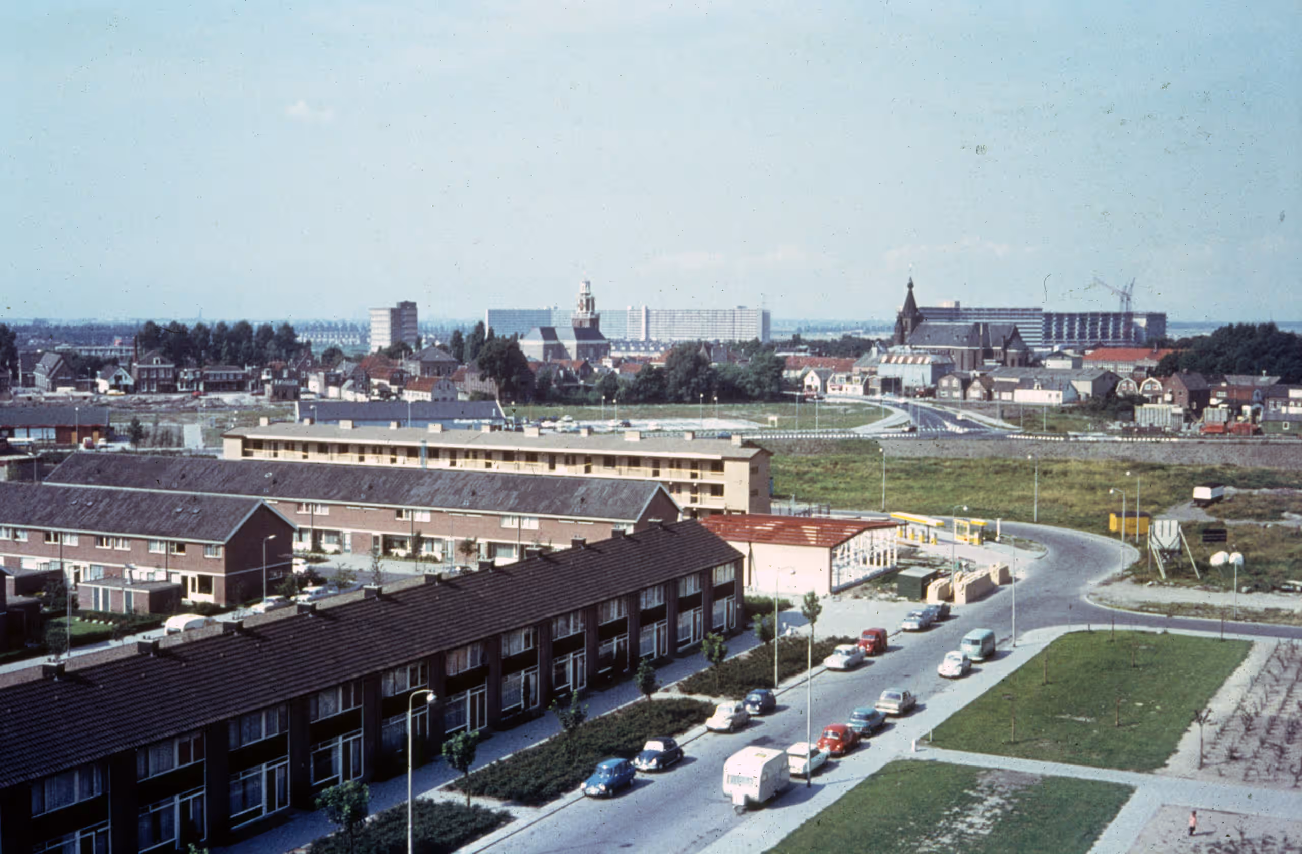 Zicht op een stad met voorin rustige wegen en woonhuizen en daarachter flats en dorpskerken.