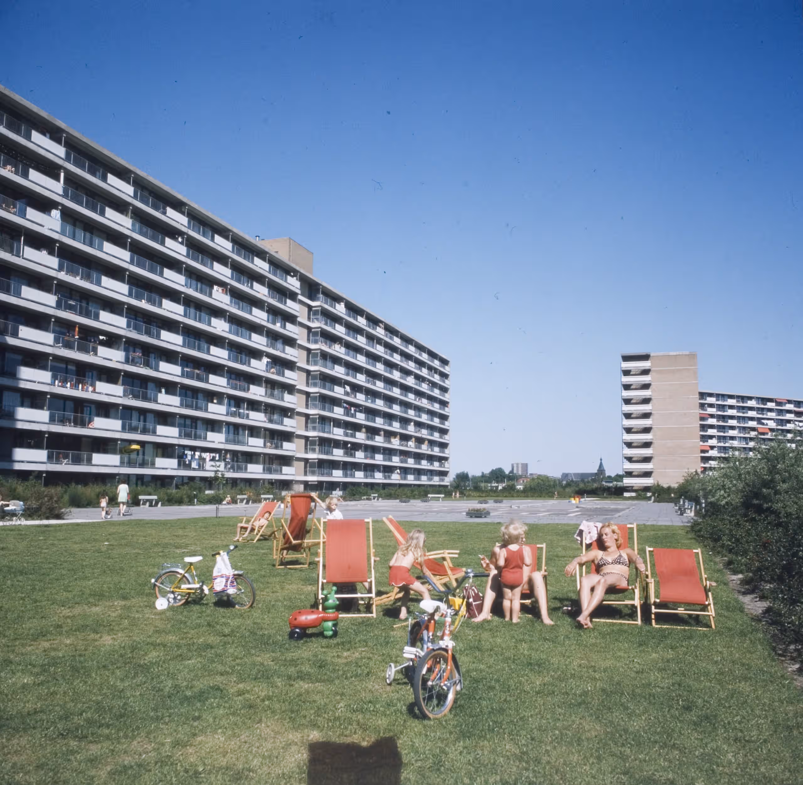 Twee flatgebouwen naast elkaar met tussenliggend stuk gras waar mensen liggen te zonnen.