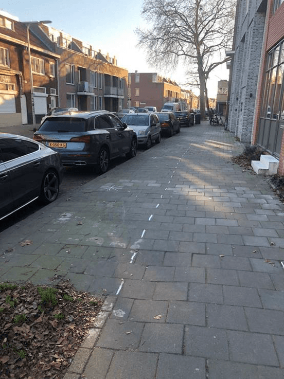 Links staan veel auto's geparkeerd, rechts een betegelde stoep.