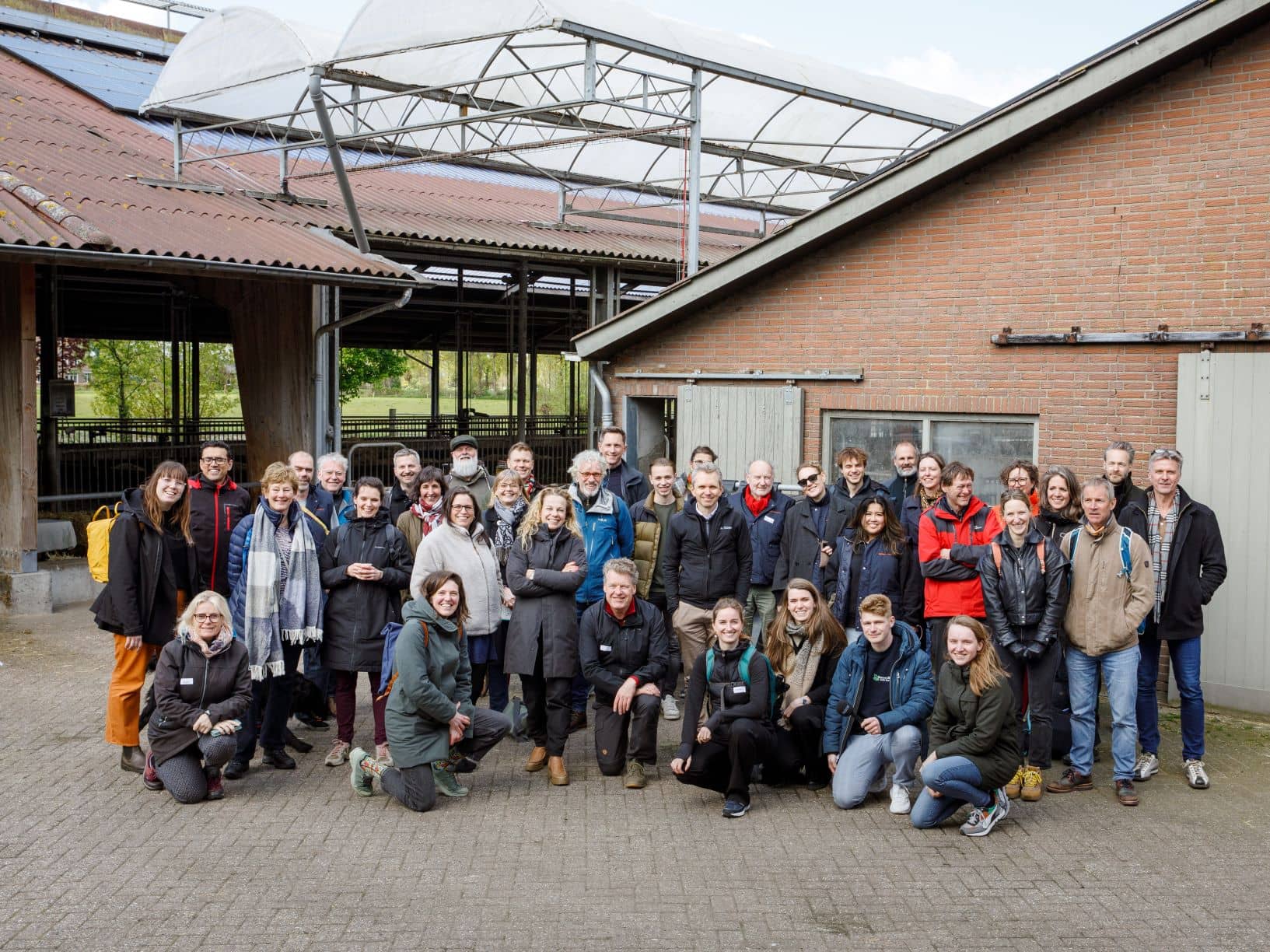 Groepsfoto van de deelnemers, ze staan voor de schuur en kijken lachend