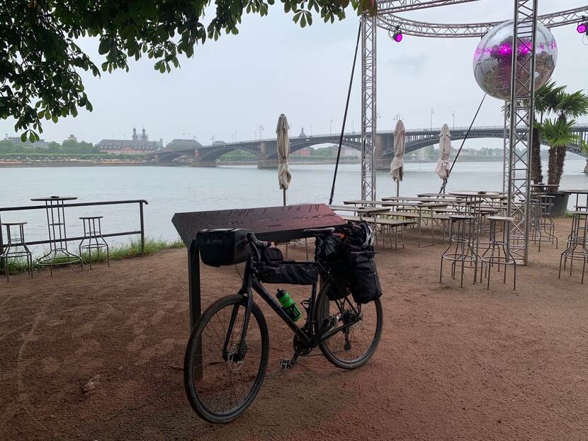Een fiets, biertafels en een discobal op de voorgrond, een rivier en brug op de achtergrond