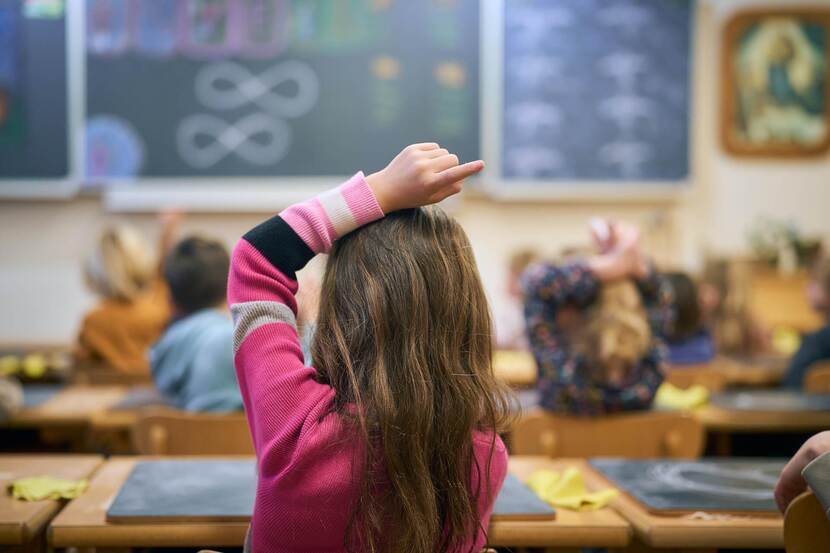 Kind in een lokaal van Vrije School Helianthus in Heerlen met haar hand omhoog