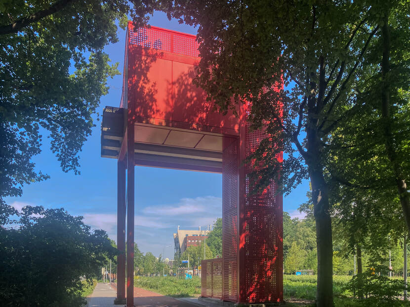 Een rood bouwwerk tussen de bomen over een fietspad heen.