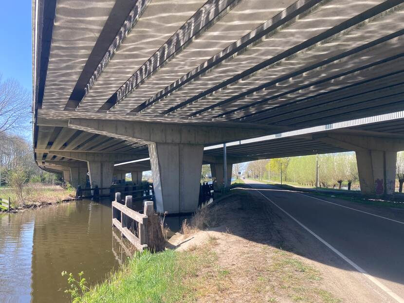 De onderkant van een brug van de snelweg, met daaronder water en een fietspad