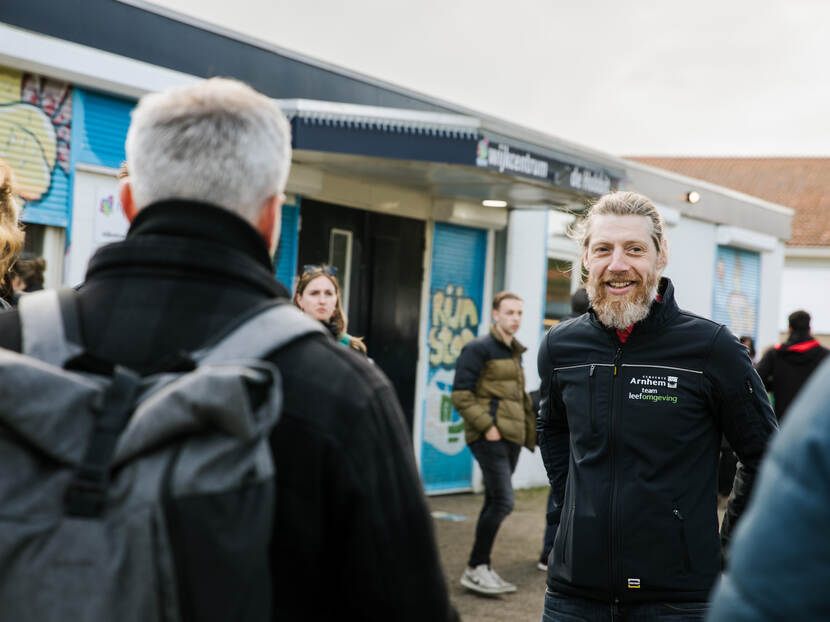 Een man met baard lachend op de foto, andere man in zijn rug gefotografeerd