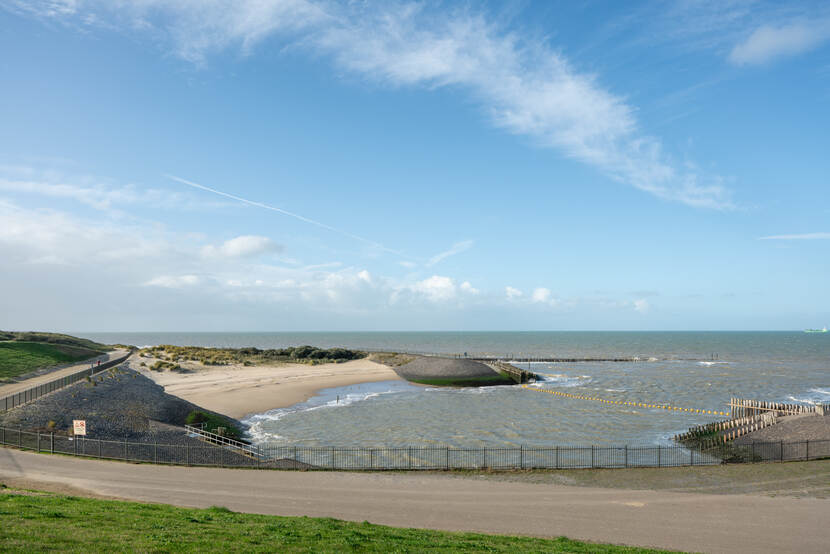 Zeewering aan een kustrand in een inkeping, de kustrand is afgezet met een hek