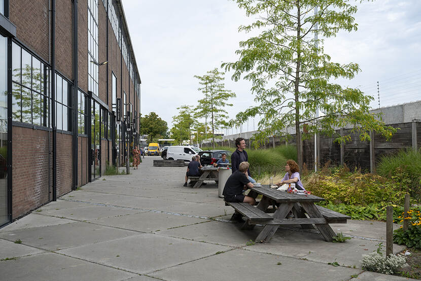 Mensen zitten aan picknicktafels op de stoep. Links het gebouw van Werkspoorfabriek.